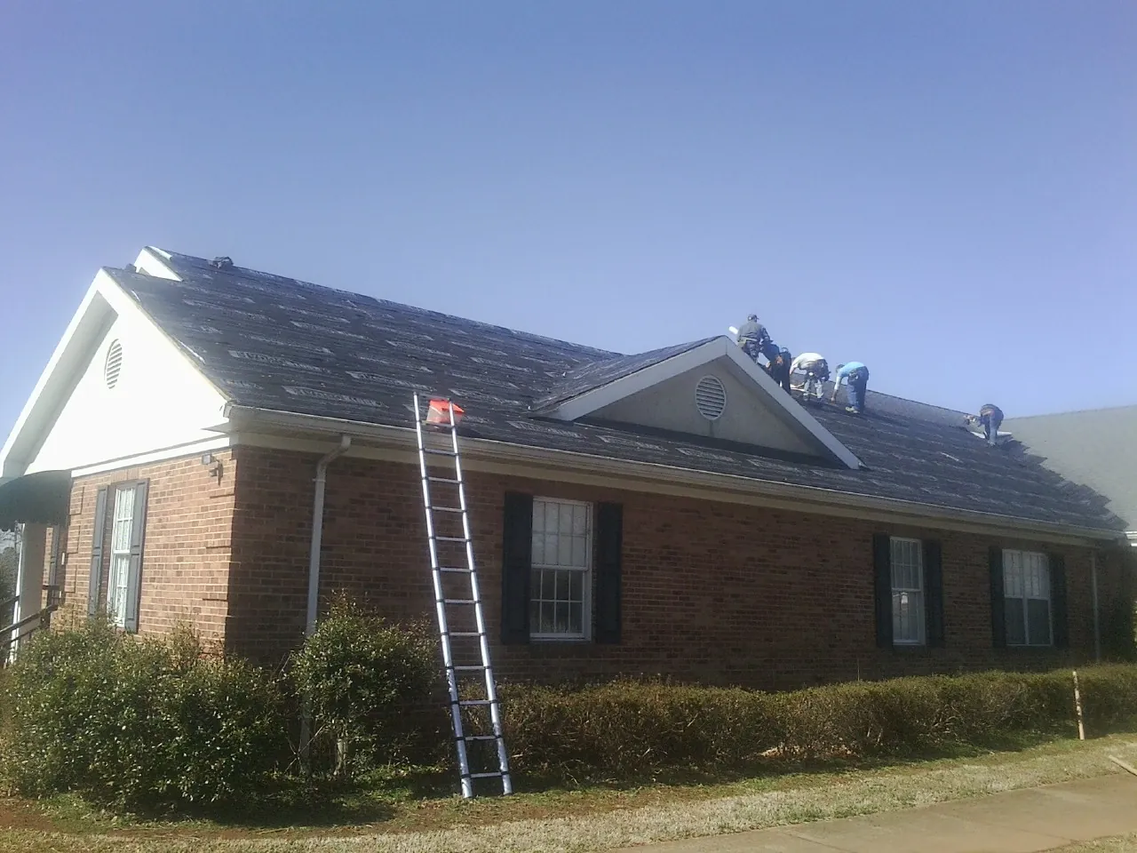 Crew tearing shingles off a brick ranch roof with a ladder set — Metal Roof Repair work by our crew in Lagunitas