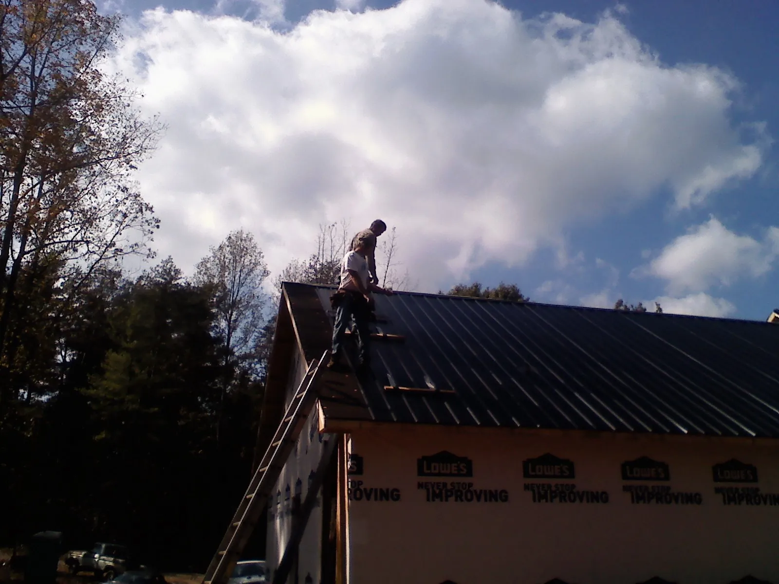 Roofer fastening dark metal panels high against a cloudy sky, from a Roof Inspection job in Lagunitas