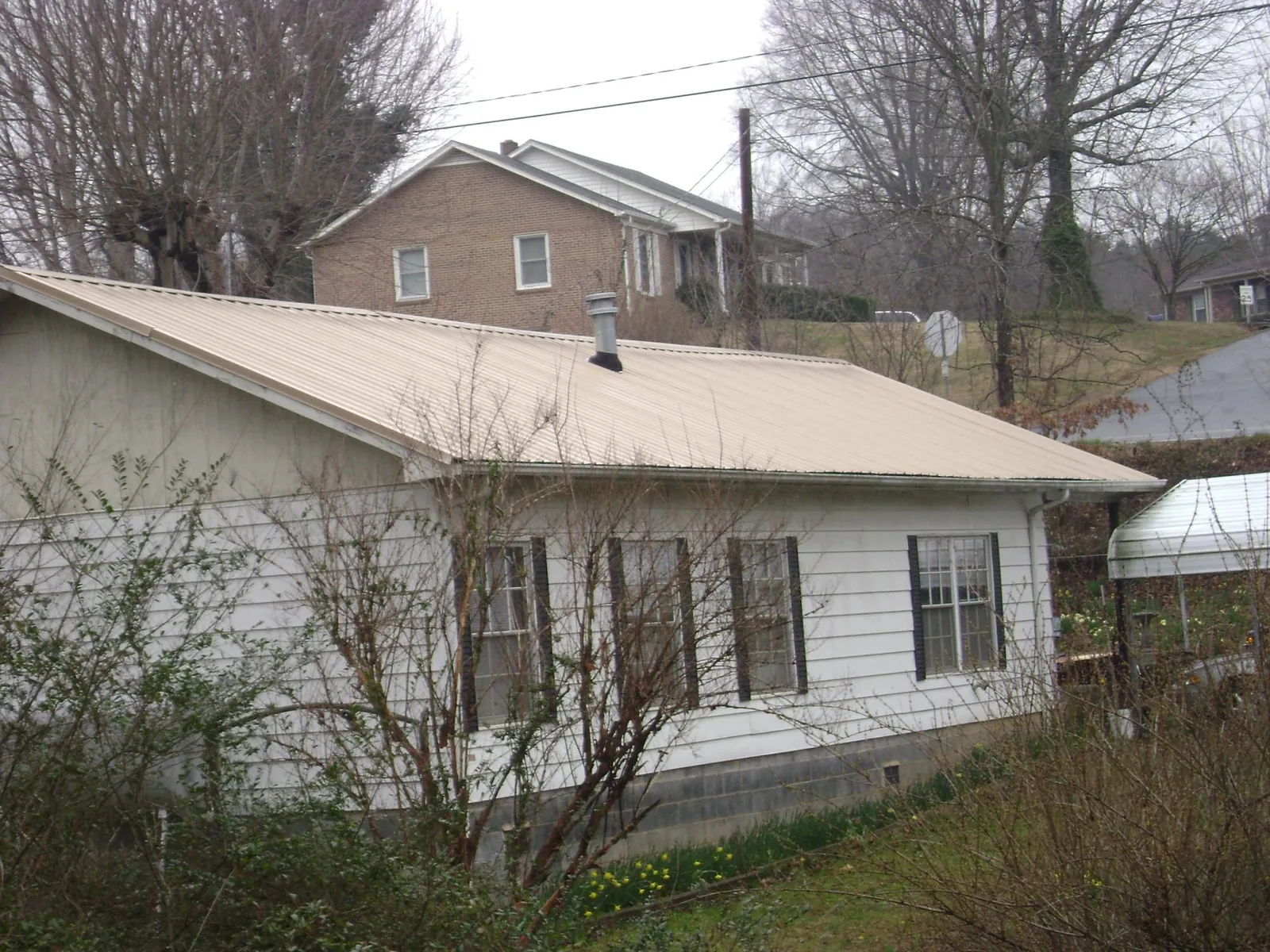 Tan metal roof on a white sided house set into a hillside — Commercial Roofing by Roofing Brothers in Lagunitas